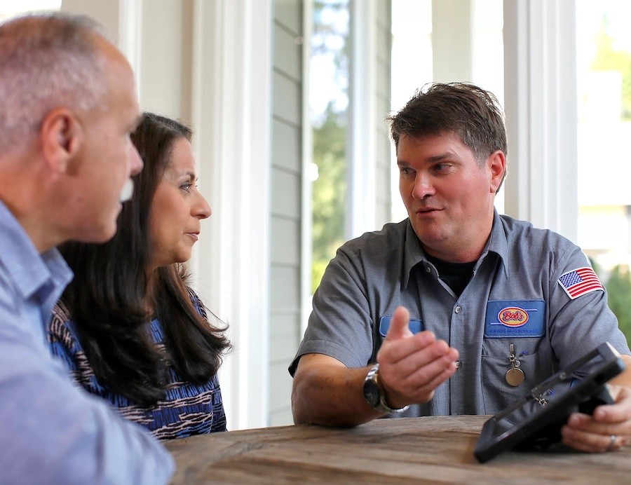 a man and woman listen to a Bob’s Heating & Air Conditioning technician while seated at a table