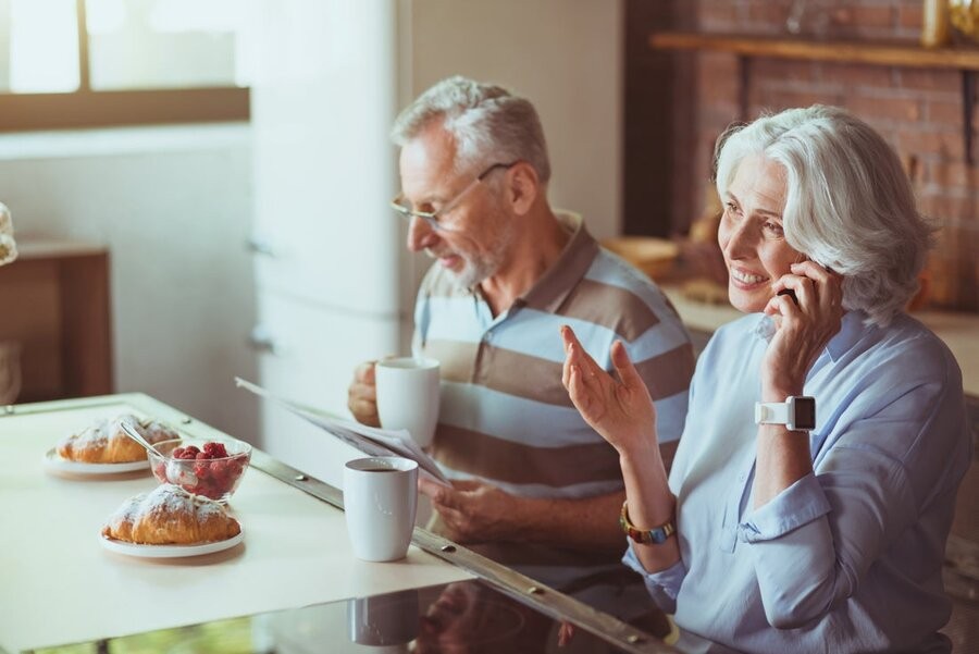 An elderly couple sitting at a home dining table drinking coffee.