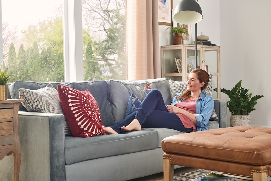 woman lounging on gray couch while enjoying an air-conditioned home in front of a window