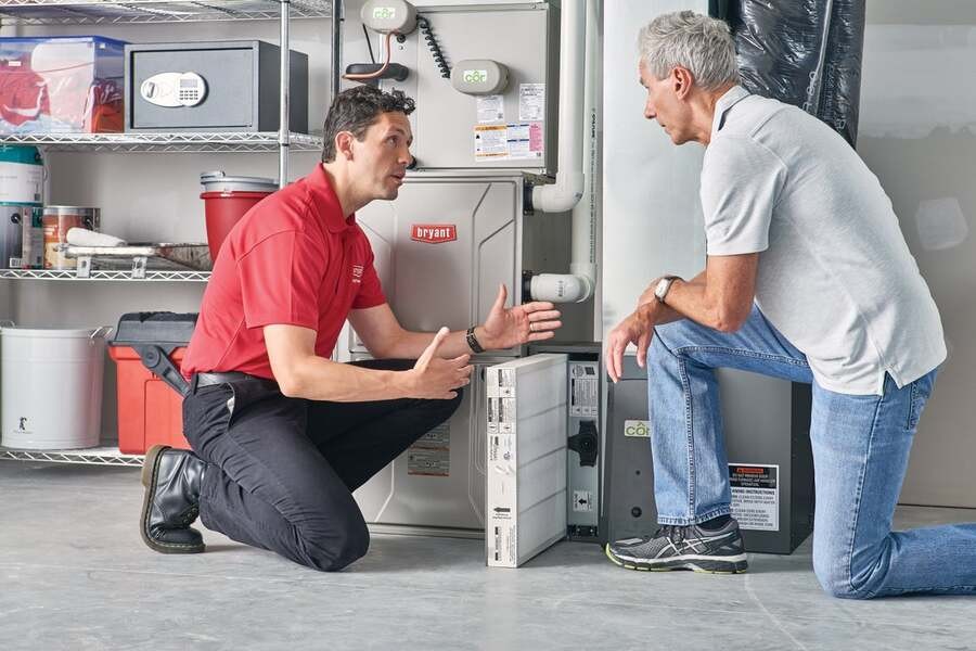 A technician provides maintenance to a HVAC system while talking to the homeowner.