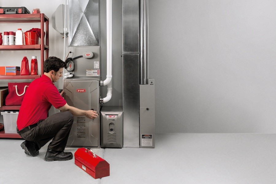 Bryant service technician wearing a red shirt and black pants while repairing a furnace