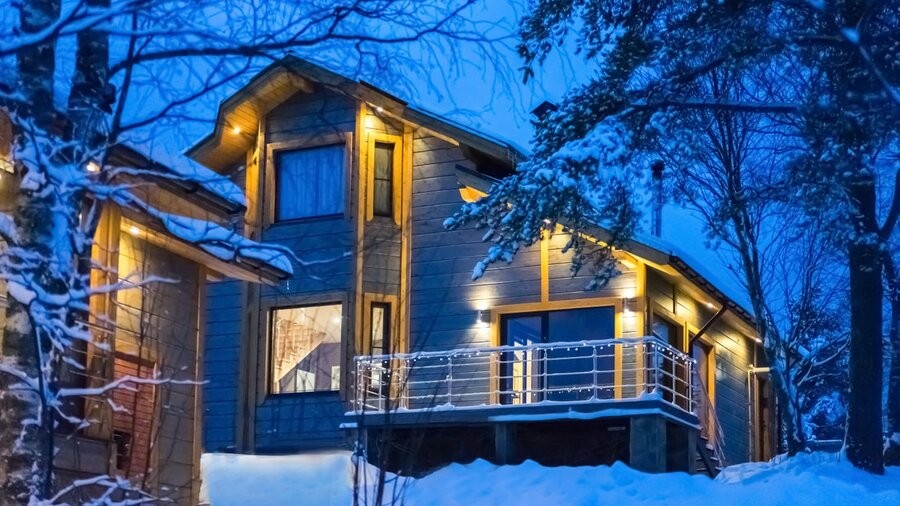 A home exterior in the snow in an area near the woods.