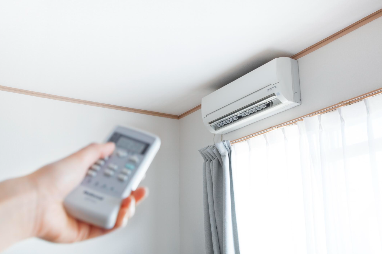 A man using a remote to control a mini-split AC unit on the wall.