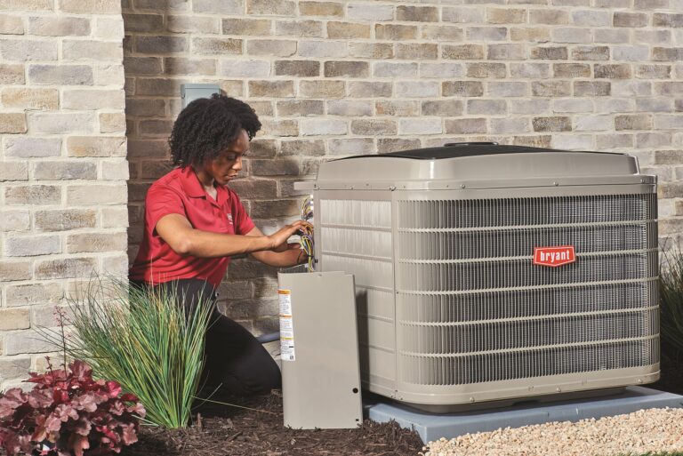 A technician working on a Bryant outdoor unit beside a brick home