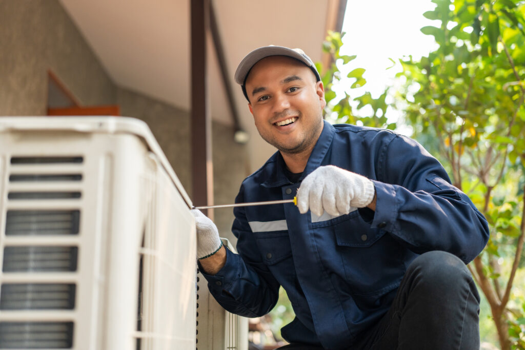 A smiling technician servicing an outdoor heat pump