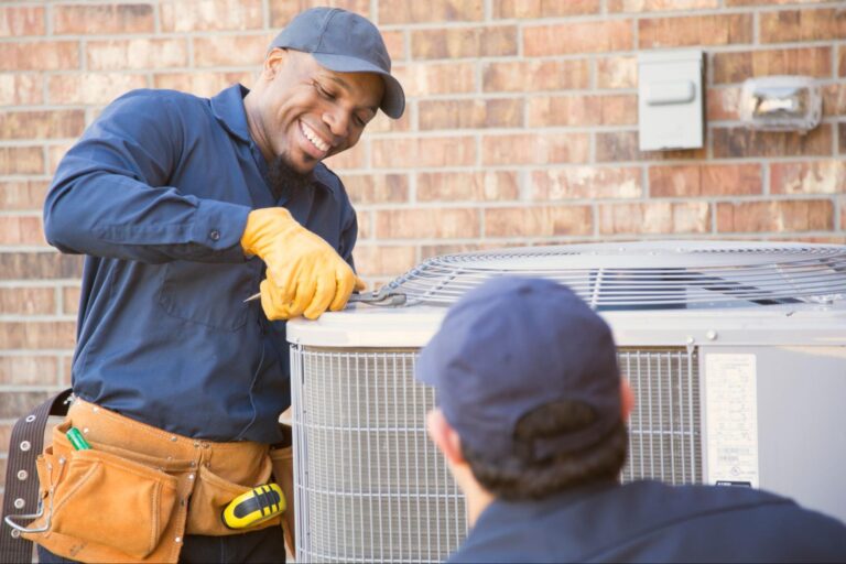 A technician servicing an outdoor unit while a colleague looks on